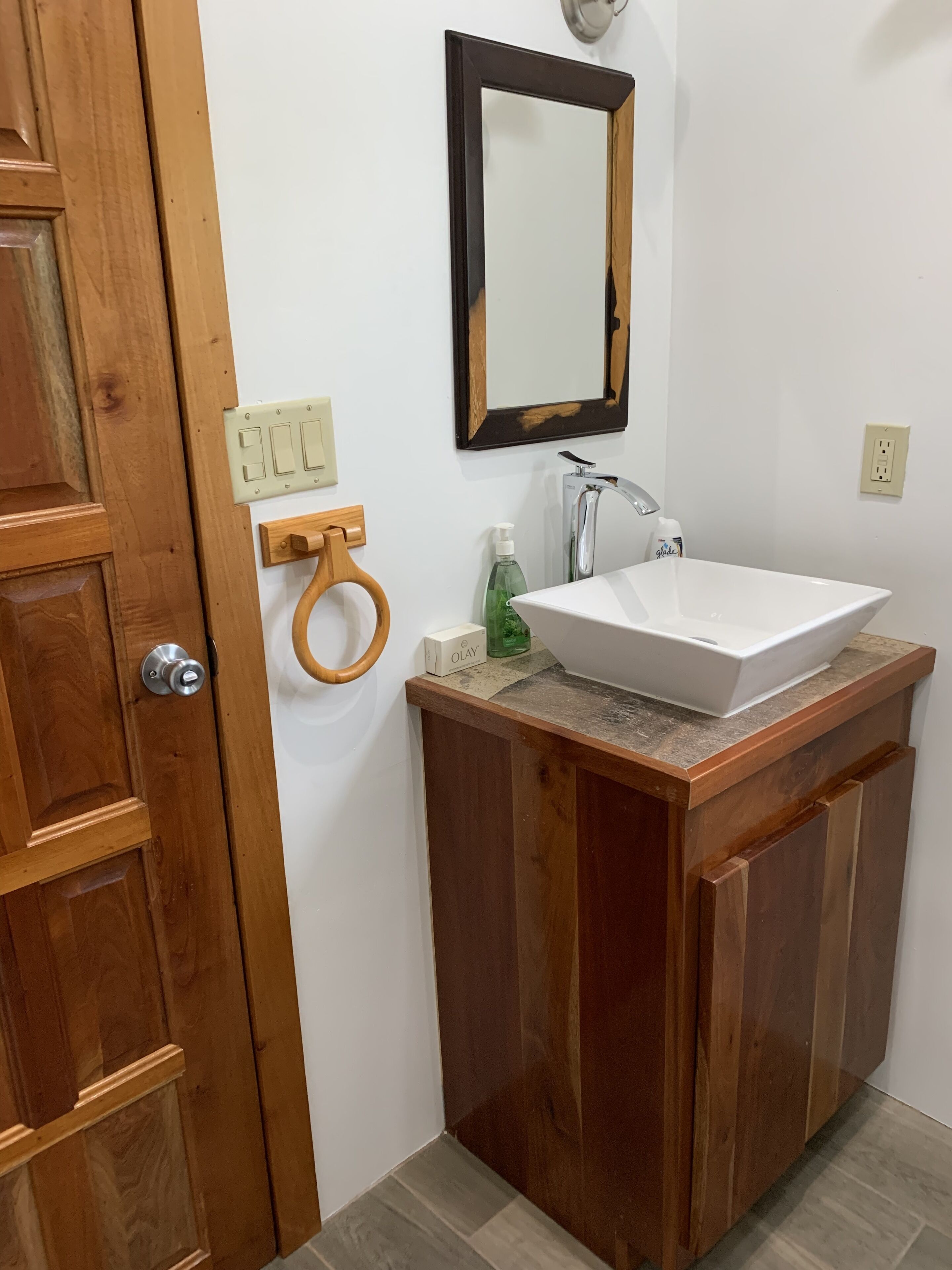 A bathroom with a wooden vanity, a white sink, a mirror, and a hand dryer.