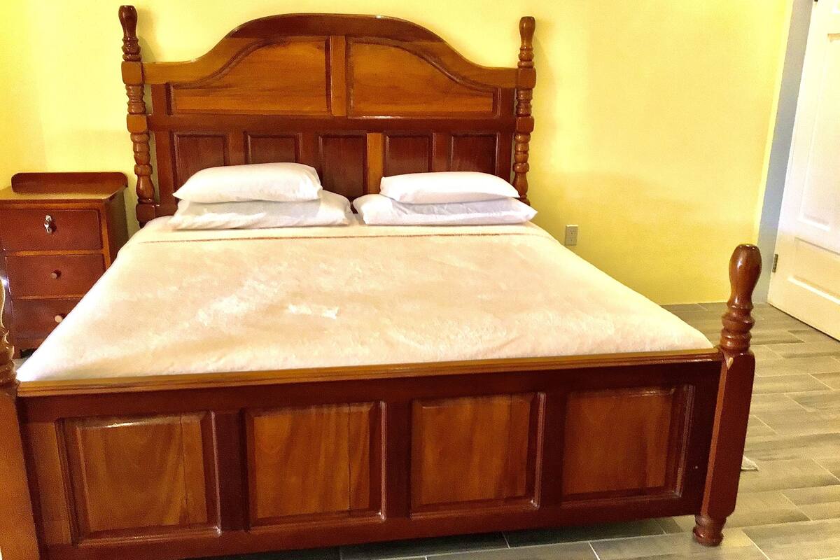 Una cama de madera con cabecera, dos almohadas y una mesita de noche a juego.