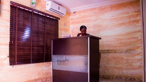 A reception area with a dark-colored desk, a window with blinds, and a tiled floor. - Glass House Suites Annex (Lagos)