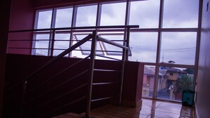 A staircase with metal railings leading to a higher floor, a large window with a view of buildings outside, and a tiled floor. - Glass House Suites Annex (Lagos)
