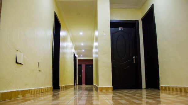 A corridor with checkered flooring, doors on both sides, and a light switch on the wall. - Glass House Suites Annex (Lagos)