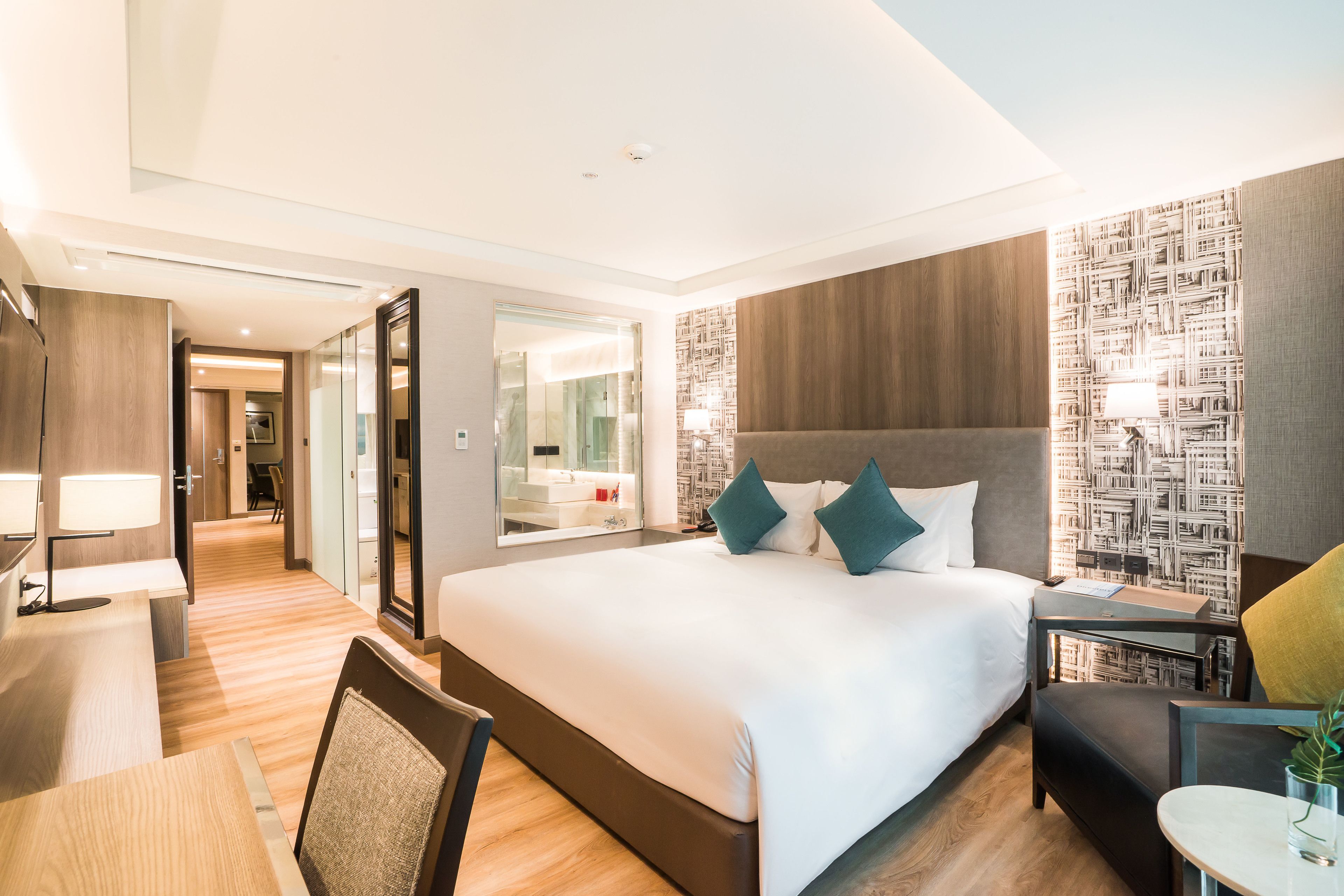 A modern hotel room with a large bed, a desk, and a chair. There is a mirror and a wall with a patterned design.