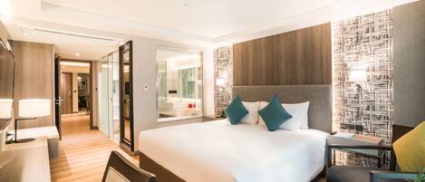 A modern hotel room with a large bed, a desk, and a chair. There is a mirror and a wall with a patterned design.