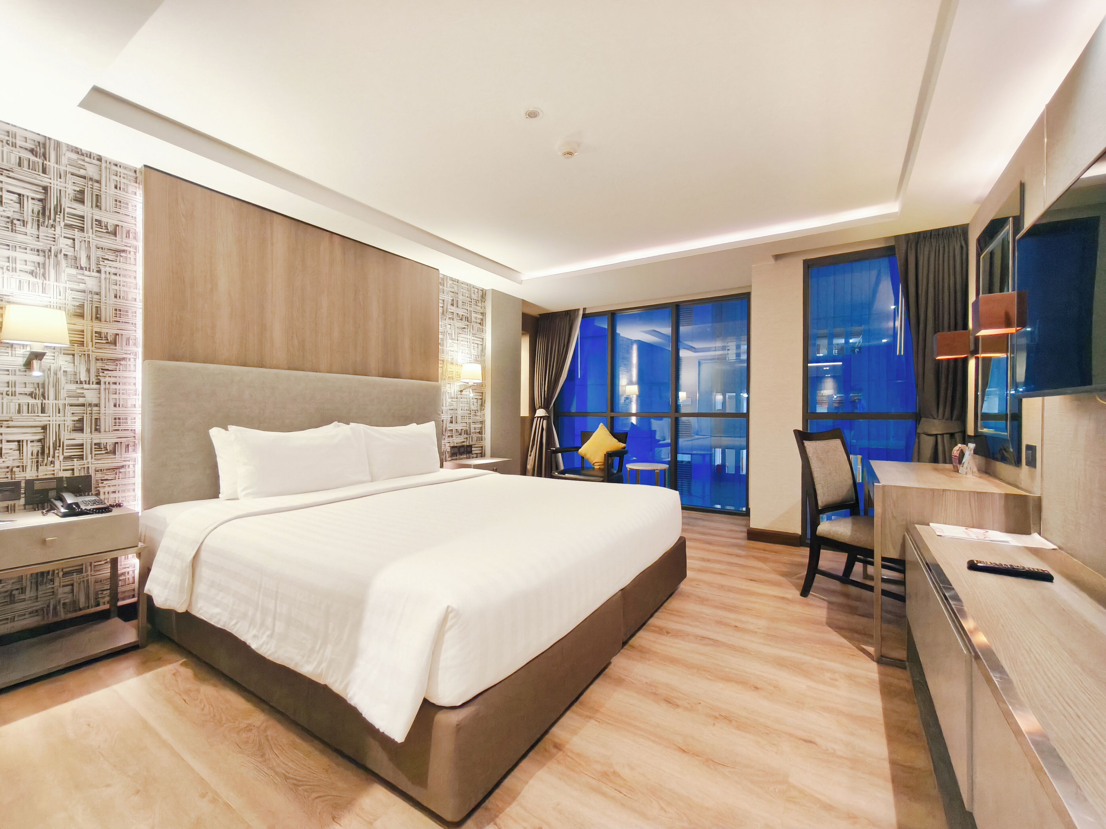 Une chambre d’hôtel moderne, dotée d’un grand lit, d’un bureau et offrant une vue sur le paysage urbain par les fenêtres.