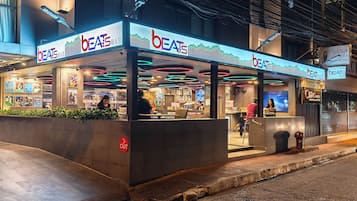 Un bar moderne, appelé « Beats Bar », aux couleurs vives, doté d’un éclairage néon et d’un espace extérieur aménagé.