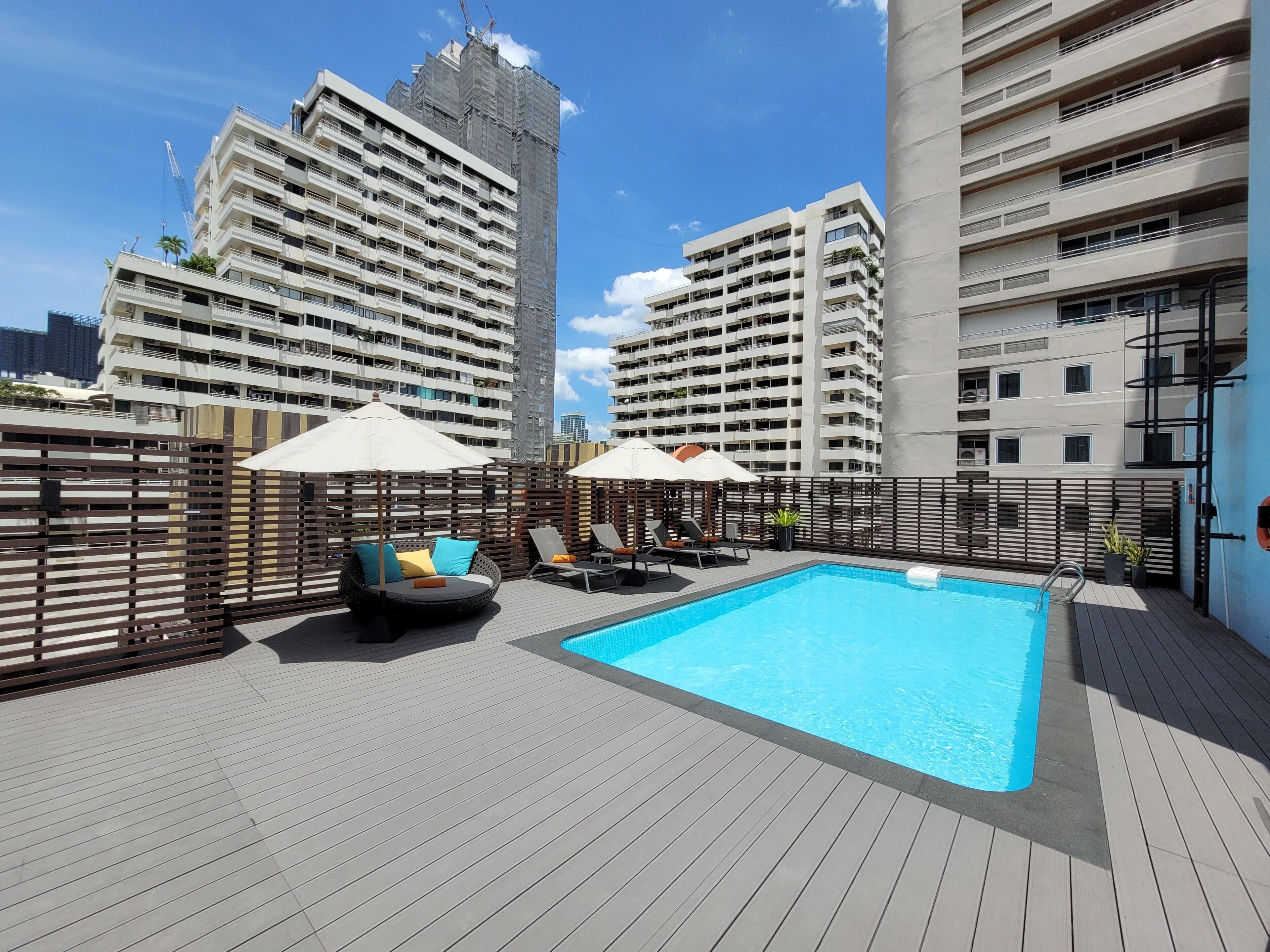A rooftop pool area with lounge chairs and umbrellas, surrounded by high-rise buildings.
