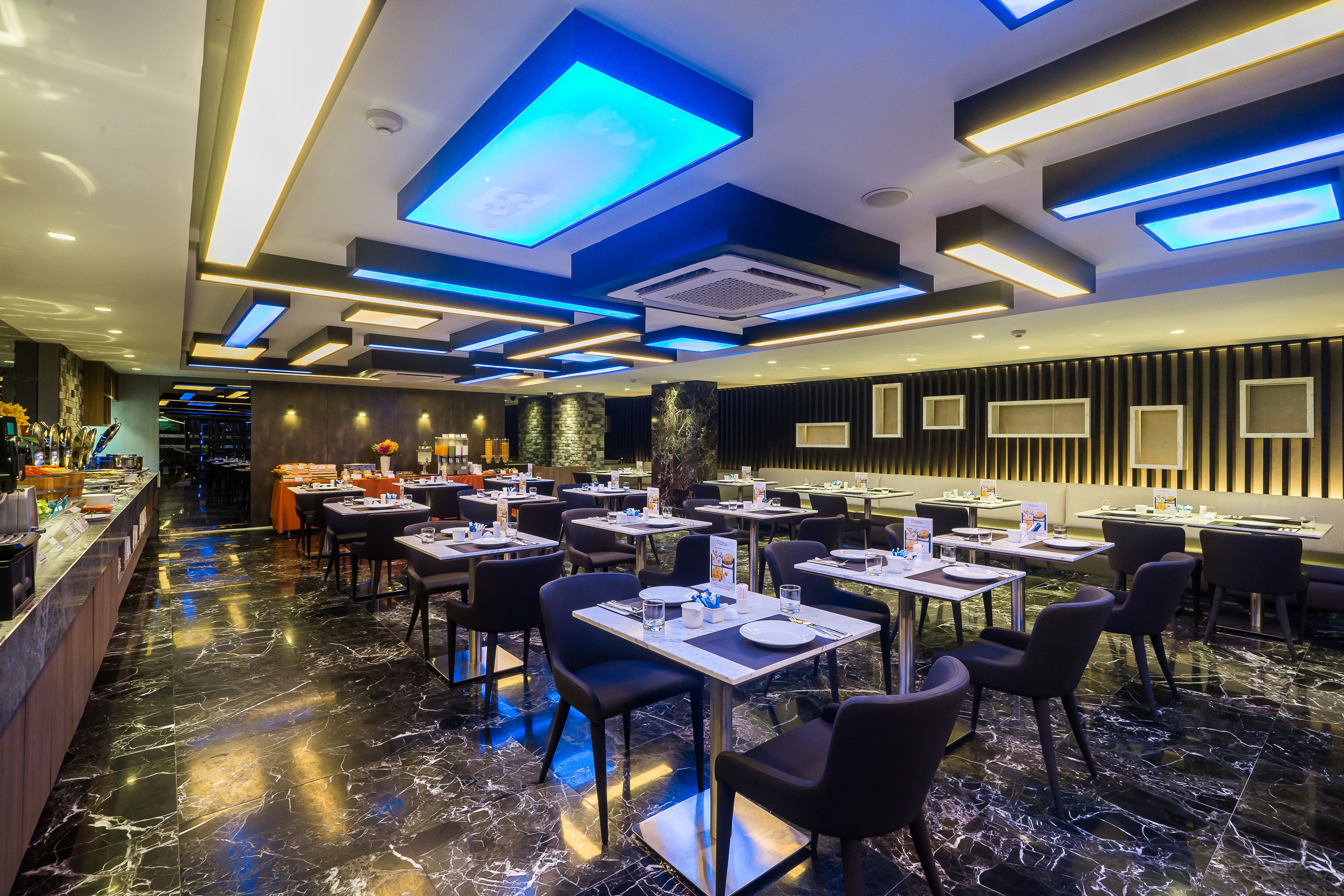 A modern restaurant with a marble floor, black and white seating, and blue ceiling lights.