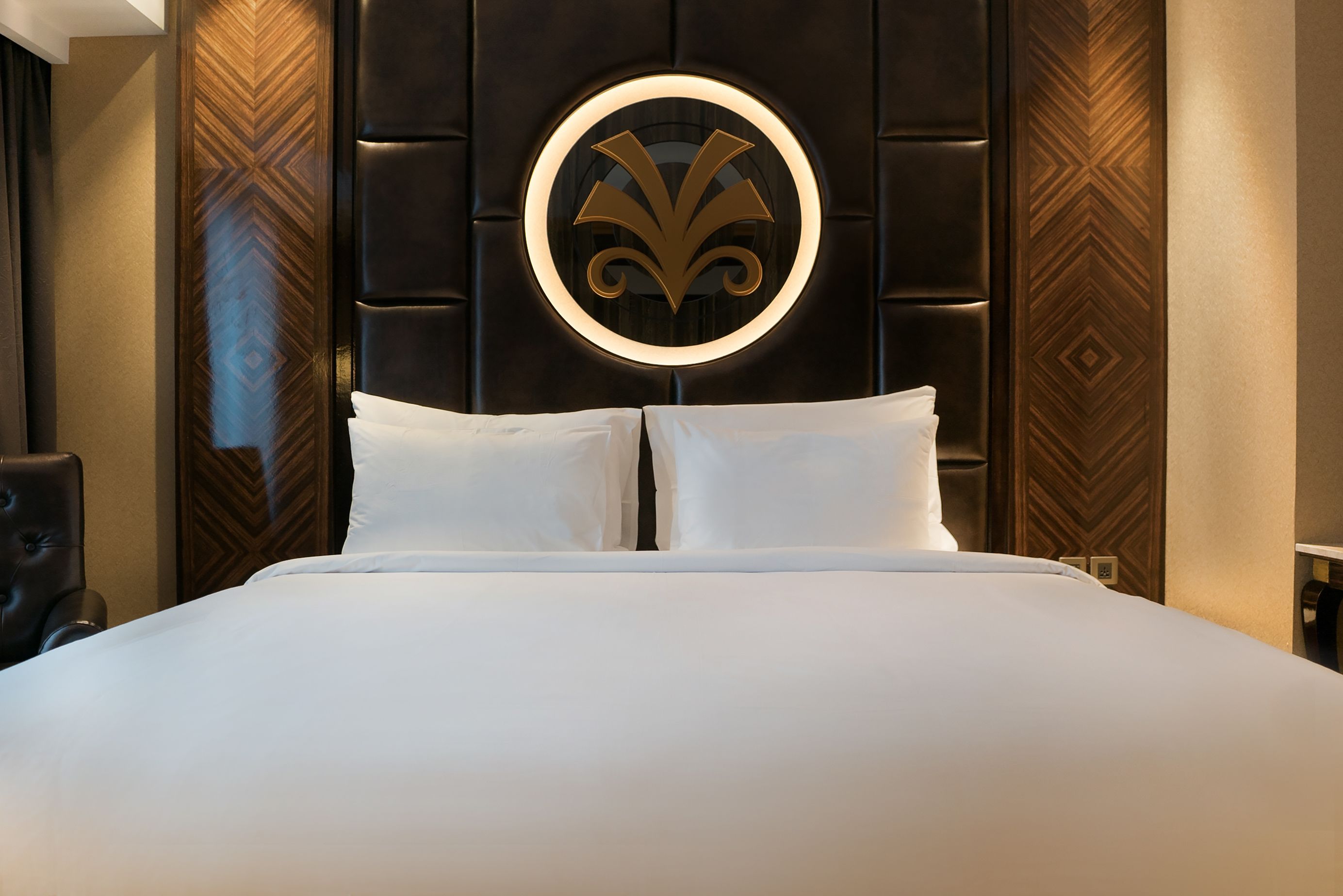 A hotel room with a large bed, a circular wall decoration, and a patterned wall panel.