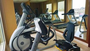 Un gimnasio con varias cintas de correr y bicicletas estáticas, ventanas amplias y un espejo grande.