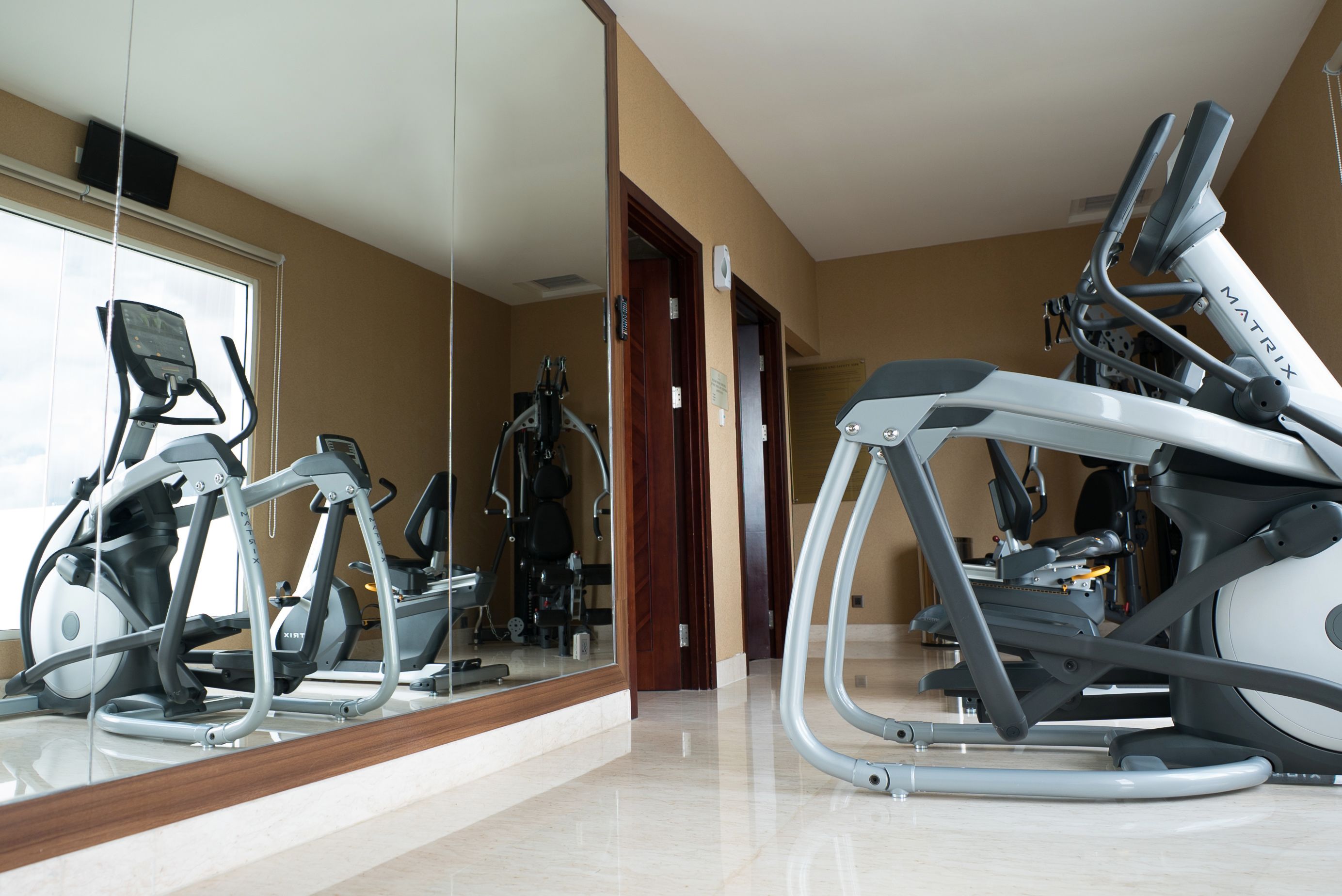 A gym with various exercise machines, a large mirror, and a wooden floor.