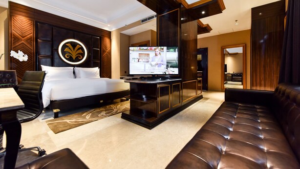 A modern hotel room with a large bed, a TV, a seating area, and a decorative wall panel. - Myko Hotel Makassar (Makassar)