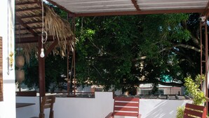 A covered outdoor seating area with wooden chairs and a table, surrounded by trees and a thatched roof structure. - Hotel Restaurant Wuarao (Boca Chica)