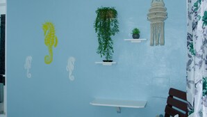 A bedroom with a blue wall, a ceiling fan, a bed with patterned pillows, a hanging macrame light, and wall decorations including a seahorse and plants. - Hotel Restaurant Wuarao (Boca Chica)