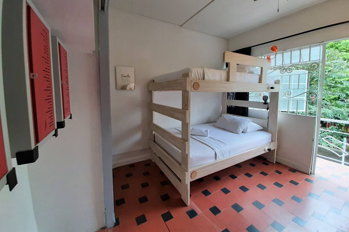 Ein Schlafraum mit Etagenbetten, einem Deckenventilator, einer Tür mit Metallgitter und einem an der Wand befestigten Schild.