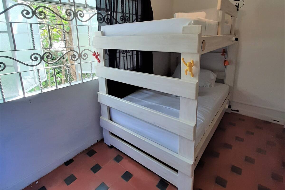 Ein Zimmer mit Etagenbett, Deckenventilator, einem Fenster mit verzierten Eisengittern und Fliesenboden.