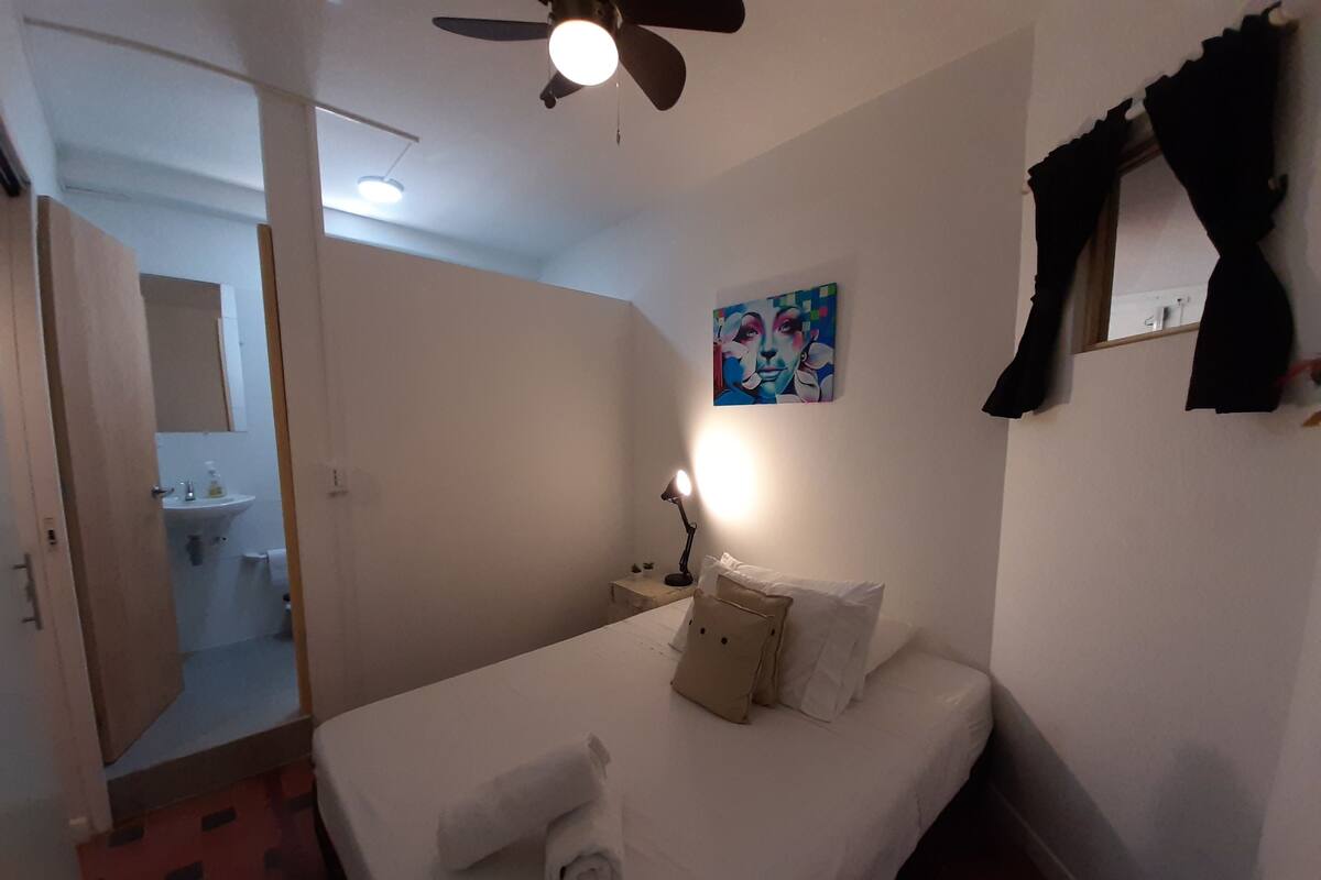 Ein Hotelzimmer mit Bett, Nachttischlampe, einem Gemälde an der Wand und einem durchgegangenen Tür sichtbaren Badezimmer.