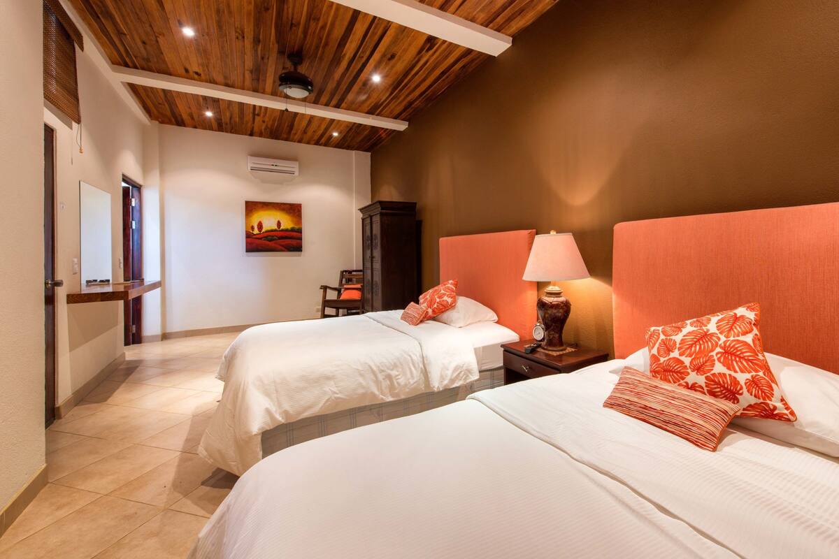 Habitación de hotel con dos camas, techo de madera, un cuadro en la pared y una mesita de noche con lámpara.