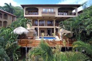 Un edificio de dos plantas con piscina, rodeado de vegetación tropical.