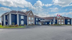 A hotel with a large parking lot, a covered entrance, and a flagpole with flags. - Quality Inn and Suites Oakville-Mississauga (Oakville)