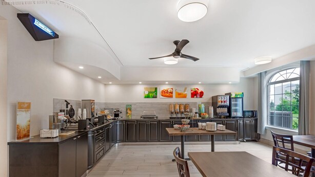 A modern kitchen with a central island, built-in appliances, and a dining area with wooden tables and chairs. - Quality Inn and Suites Oakville-Mississauga (Oakville)