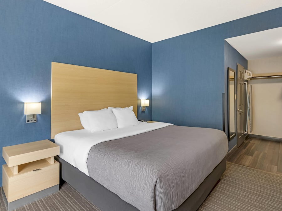 Quarto de hotel com uma cama grande, cabeceira de madeira, duas mesas de cabeceira com luminárias e um closet espaçoso com chuveiro.