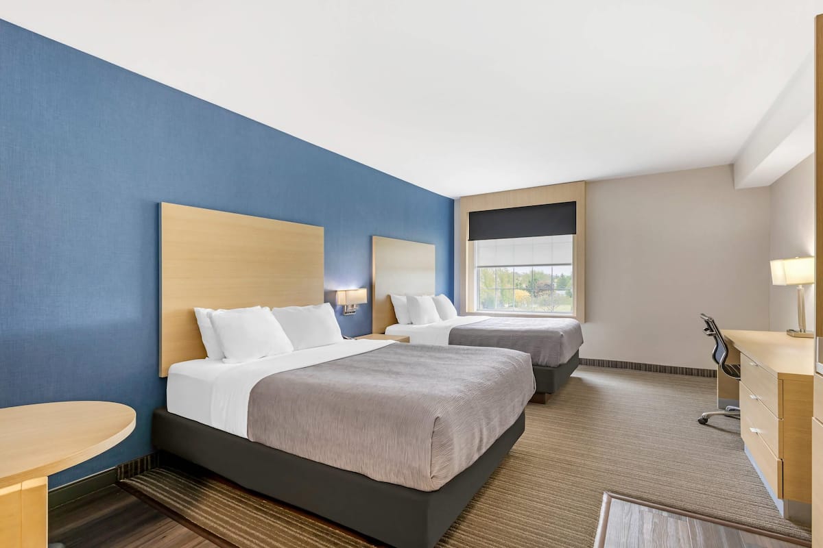 Habitación de hotel con dos camas, un escritorio, una silla y una ventana con vistas.
