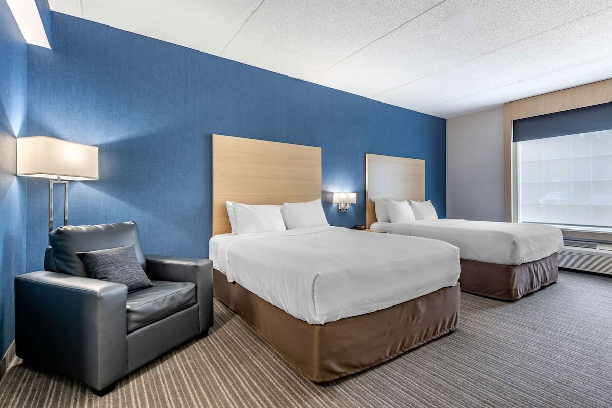 Habitación de hotel con dos camas, un sofá, una lámpara y un ventanal grande.