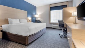 A hotel room with a large bed, a desk with a computer, a chair, a TV, and a window with blinds. - Quality Inn and Suites Oakville-Mississauga (Oakville)