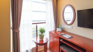 A hotel room with a large window, a flat-screen TV, a wooden desk, a small table with a plant, and a mirror on the wall. - GreenTree Inn Suzhou Kunshan Paris Spring Express Hotel (Suzhou)