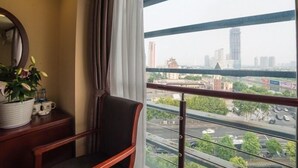A hotel room with a view of a cityscape, a chair, a small table with a potted plant, and a window with curtains. - GreenTree Inn Suzhou Kunshan Paris Spring Express Hotel (Suzhou)