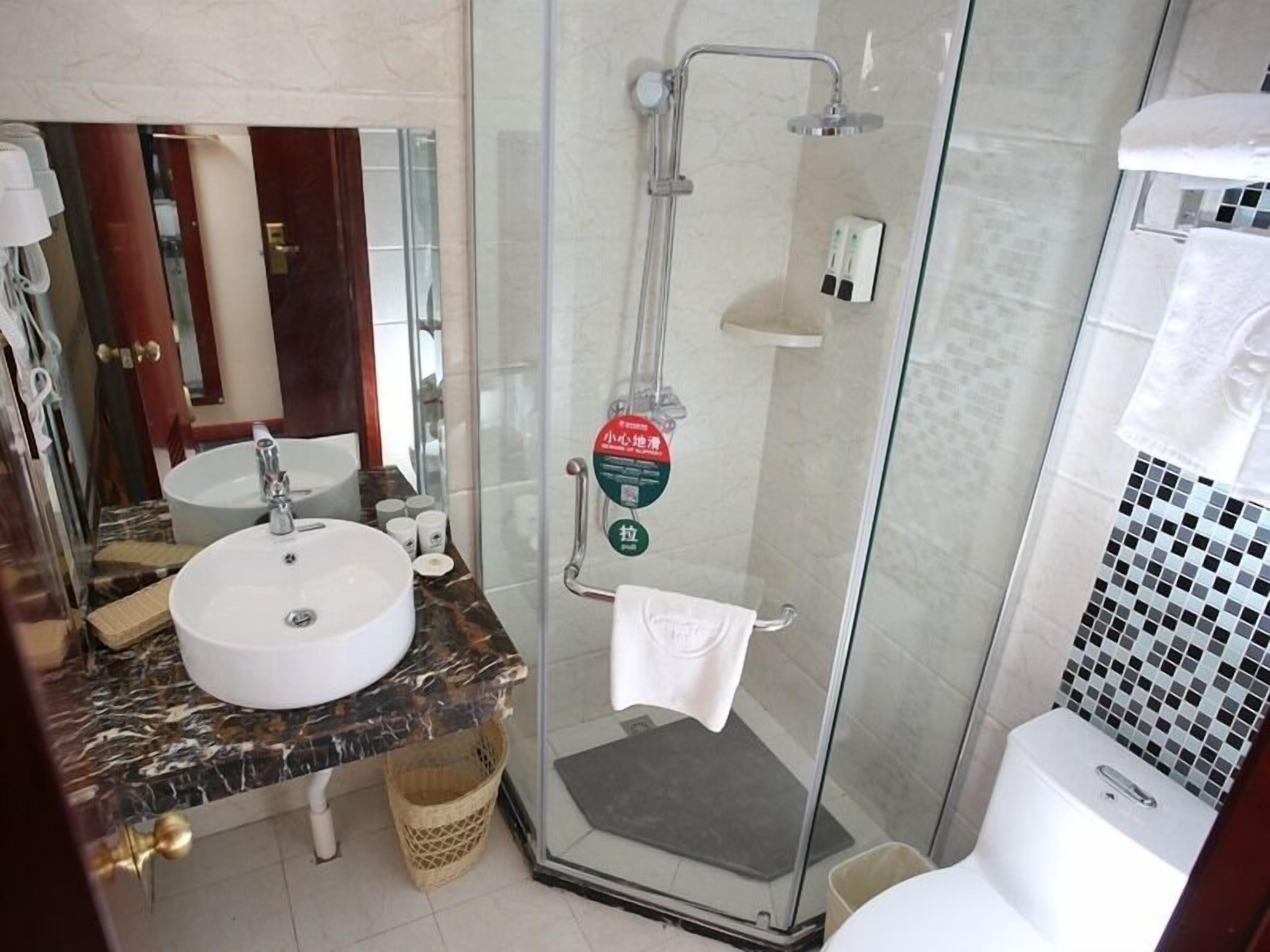 A bathroom with a glass-enclosed shower, a sink with a marble countertop, and a toilet with a mosaic tile backsplash.
