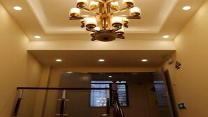 Un candelabro con múltiples lámparas, una escalera con barandillas de vidrio y una luz empotrada en el techo.