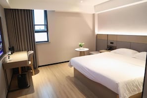 Habitación de hotel con cama, escritorio, silla, una mesita con planta y ventana con cortinas.
