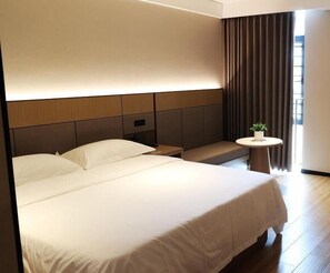 A modern hotel room with a large bed, a bedside table, a small round table with a plant, and a view of the outdoors through curtains. - Greentree Inn Mong Kok Express Hote (Suzhou)