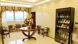 A hotel lobby with a round table, chairs, a large vase of flowers, a bookshelf, and a view of the outdoors. - Greentree Inn Mong Kok Express Hote (Suzhou)
