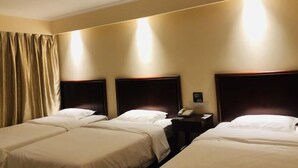 Habitación de hotel con cuatro camas individuales, una mesita de noche con teléfono y una lámpara fijada a la pared.