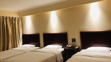 Ein Hotelzimmer mit vier Einzelbetten, einem Nachttisch mit Telefon und einer Wandleuchte.