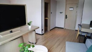 Una habitación de hotel moderna con televisión de pantalla plana, una planta pequeña, un sofá y un escritorio.