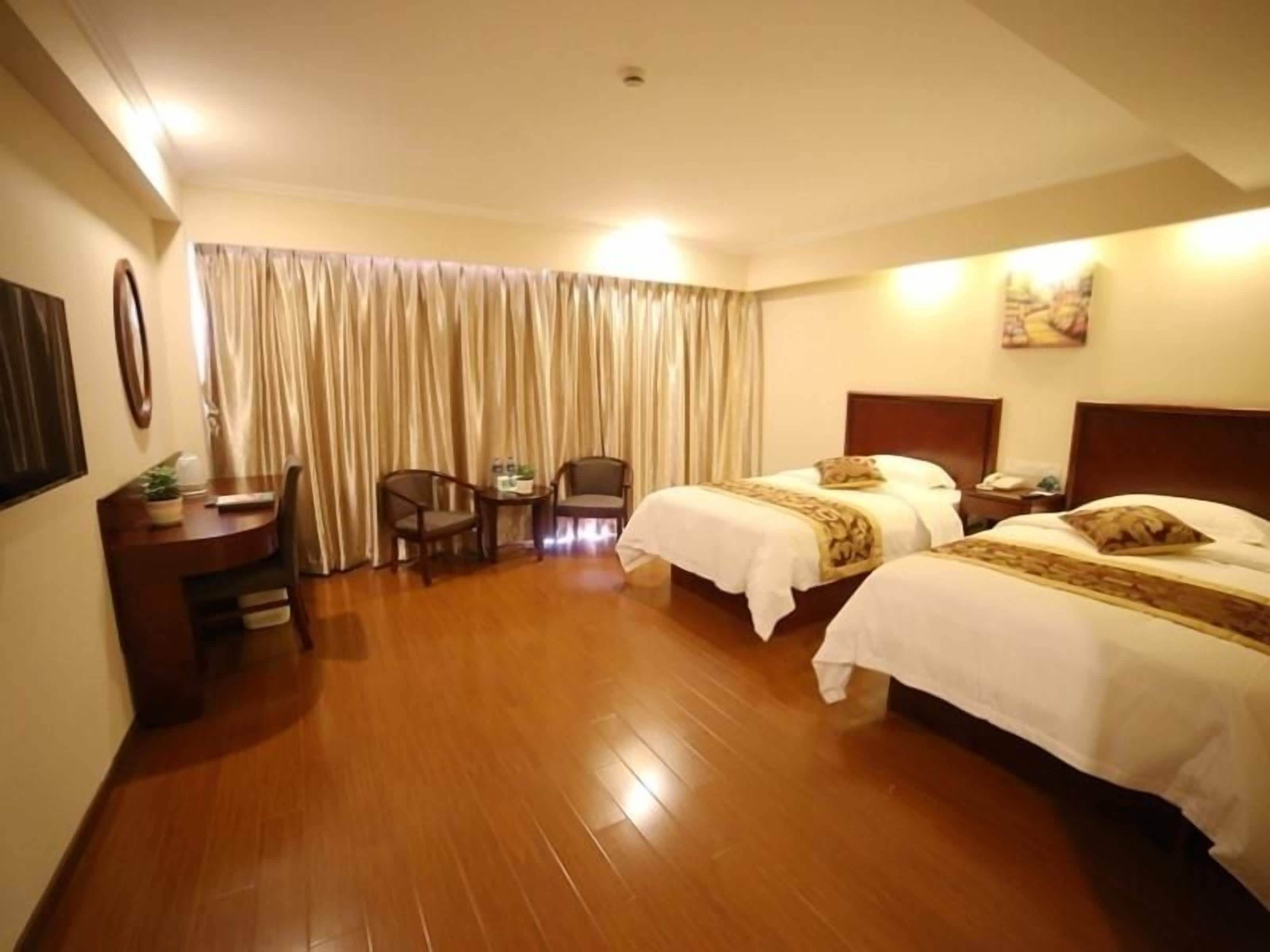 A hotel room with two beds, a desk, a chair, and a large window with curtains.