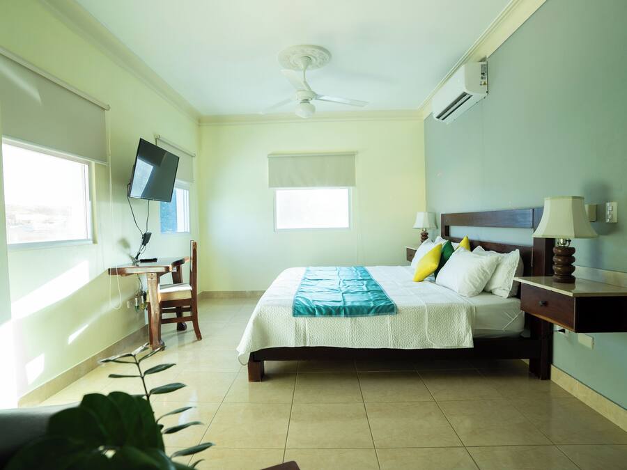 Un dormitorio con cama, escritorio, silla, televisor y ventilador de techo.