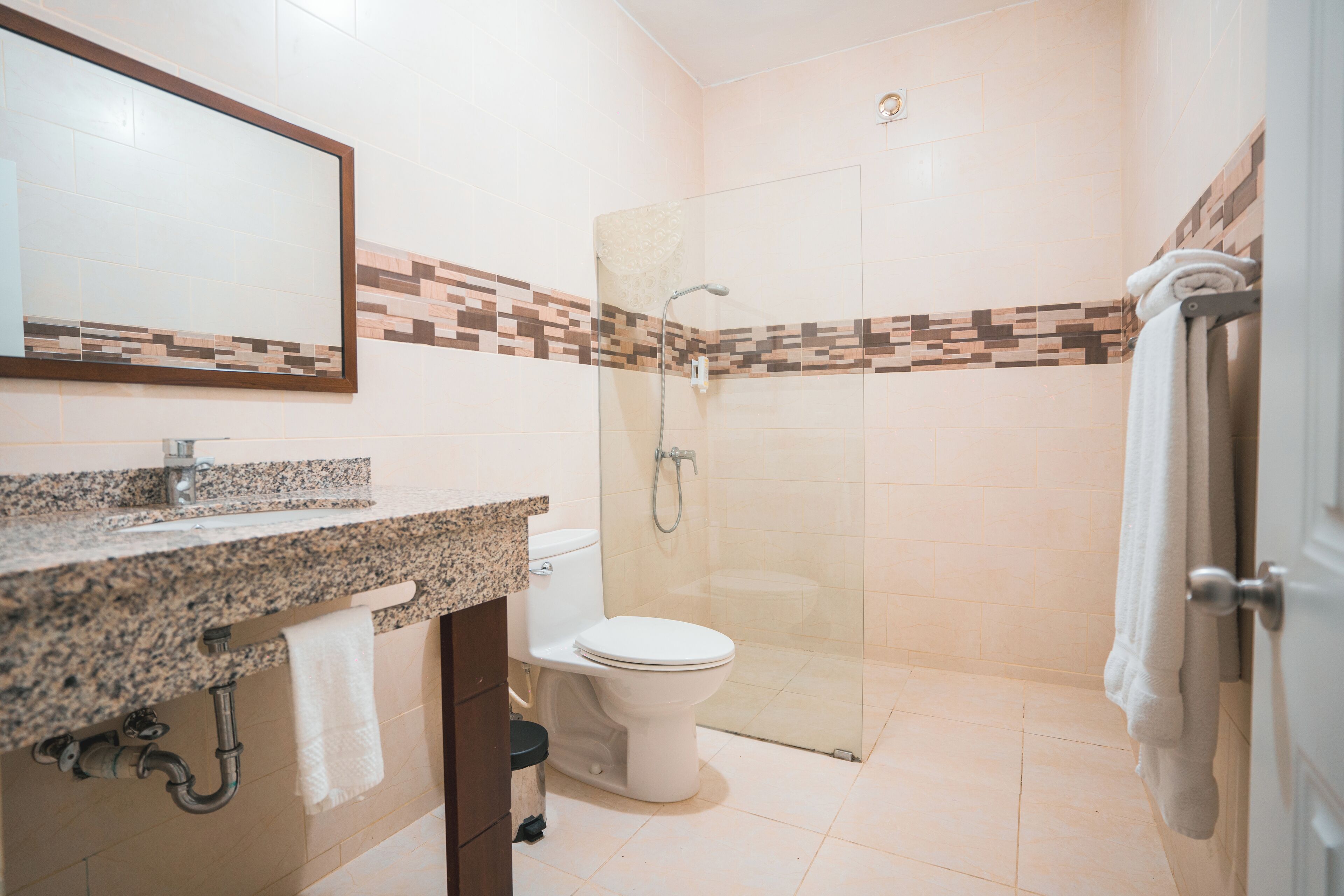 Un baño con encimera de granito, inodoro, cabina de ducha de vidrio y toallero.