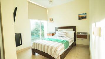 Quarto com cama, mesa de cabeceira, televisão na parede, janela e ventilador de teto.