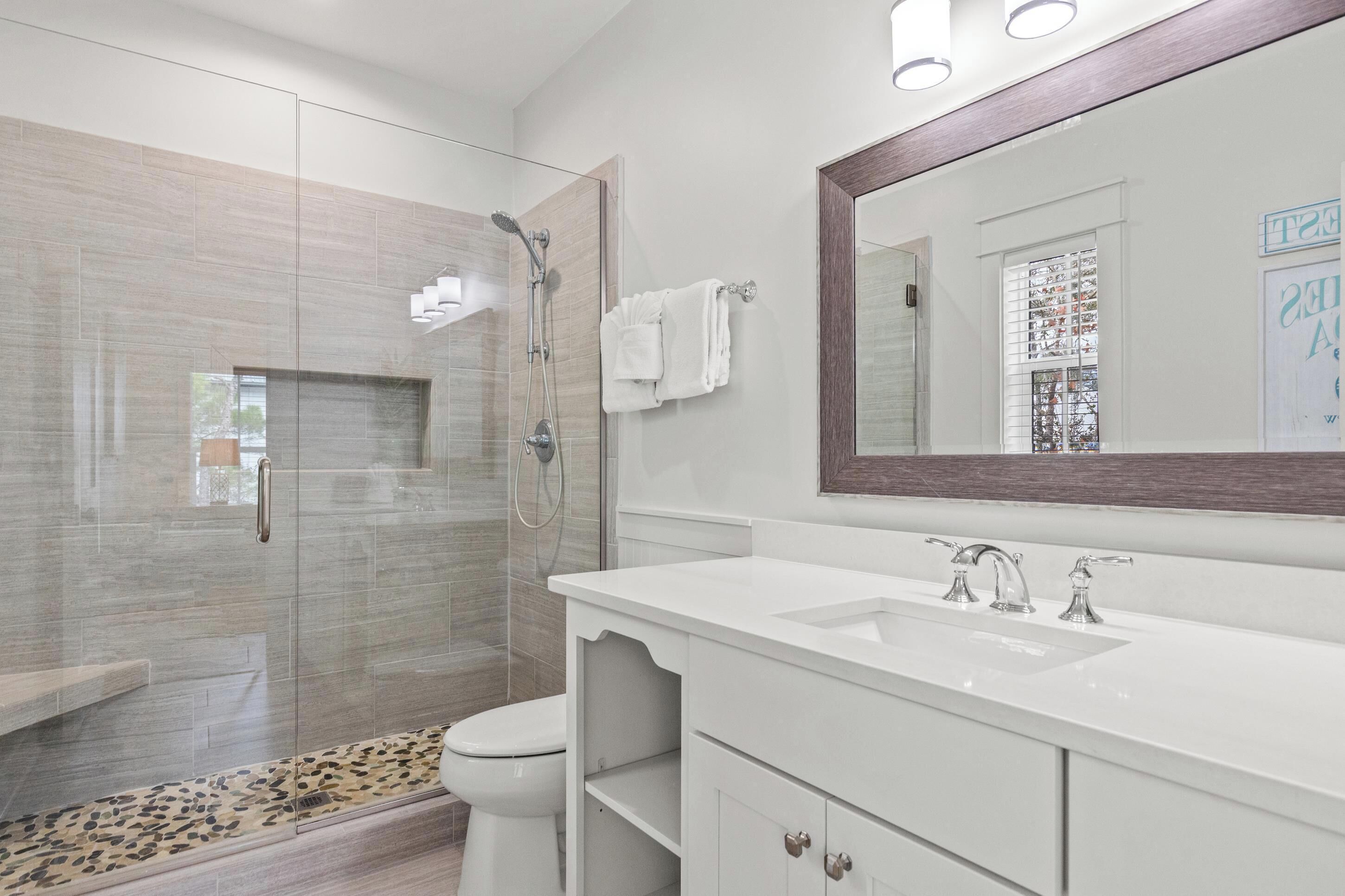 Une salle de bain moderne avec une douche à parois de verre, un lavabo blanc doté de deux robinets et un grand miroir.