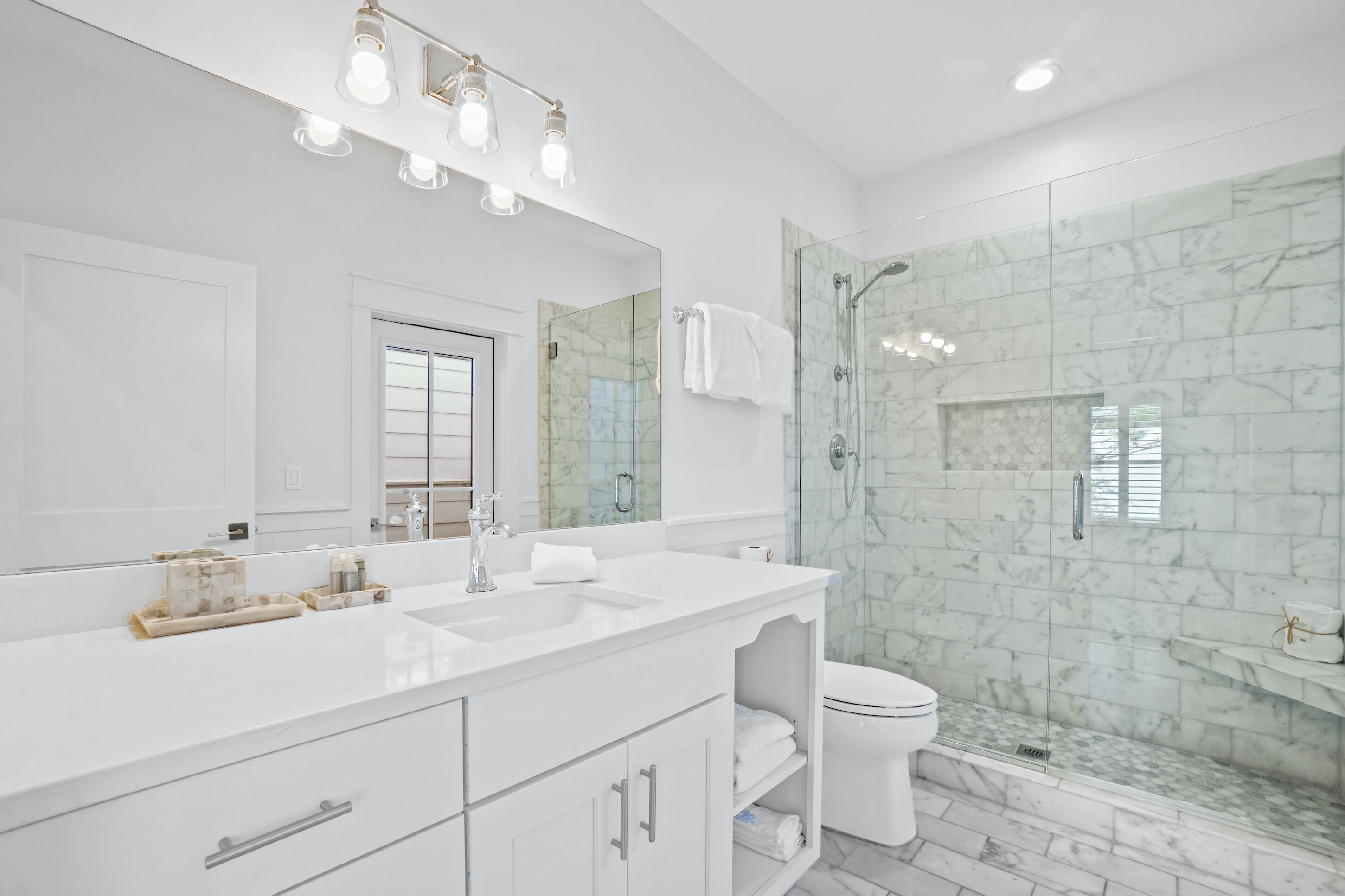 A modern bathroom with a large mirror, white vanity, and a glass-enclosed shower area.