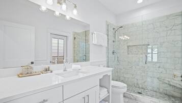 A modern bathroom with a large mirror, white vanity, and a glass-enclosed shower area.