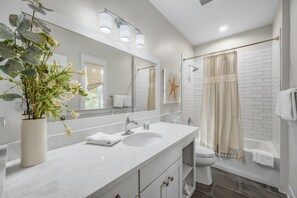 A modern bathroom with a white sink, large mirror, and a shower with a beige curtain. - Magnolia Cottages by the Sea by Panhandle Getaways (Panama City Beach)