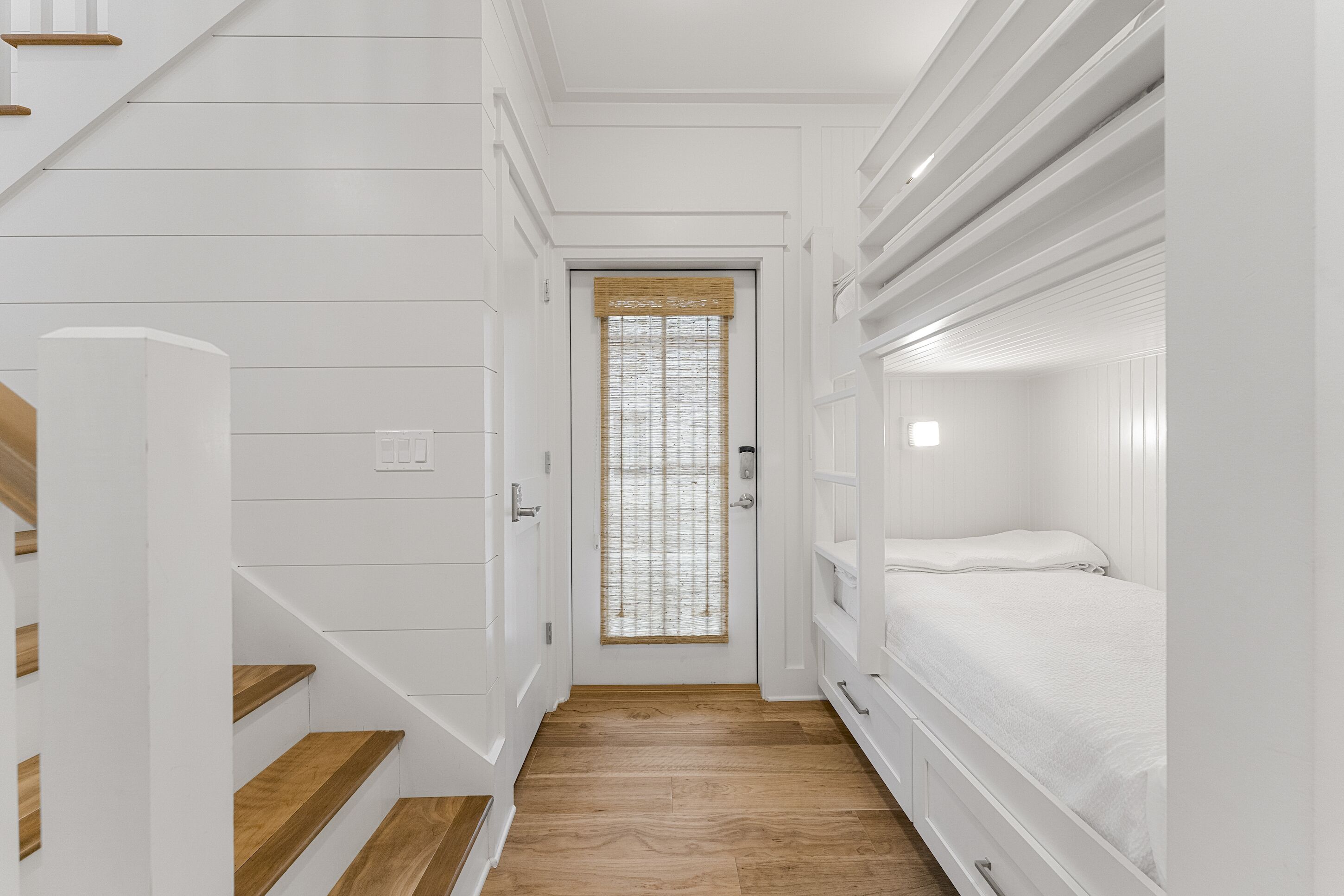 Un couloir étroit, avec un escalier en bois sur la gauche et un lit superposé sur la droite.