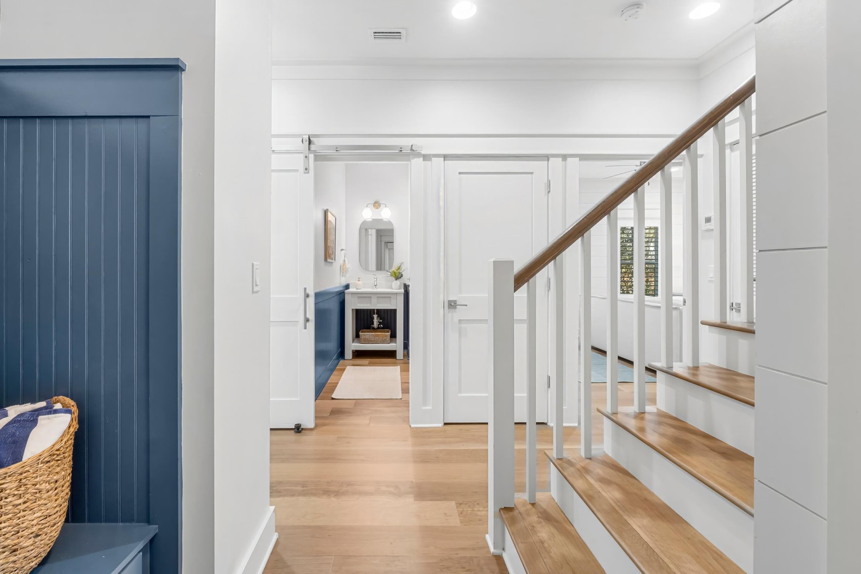 A hallway with a wooden staircase, white walls, and a blue door.