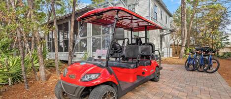 Un carrito de golf rojo estacionado sobre un camino de ladrillo frente a una casa con un ventanal grande y un porche cubierto.