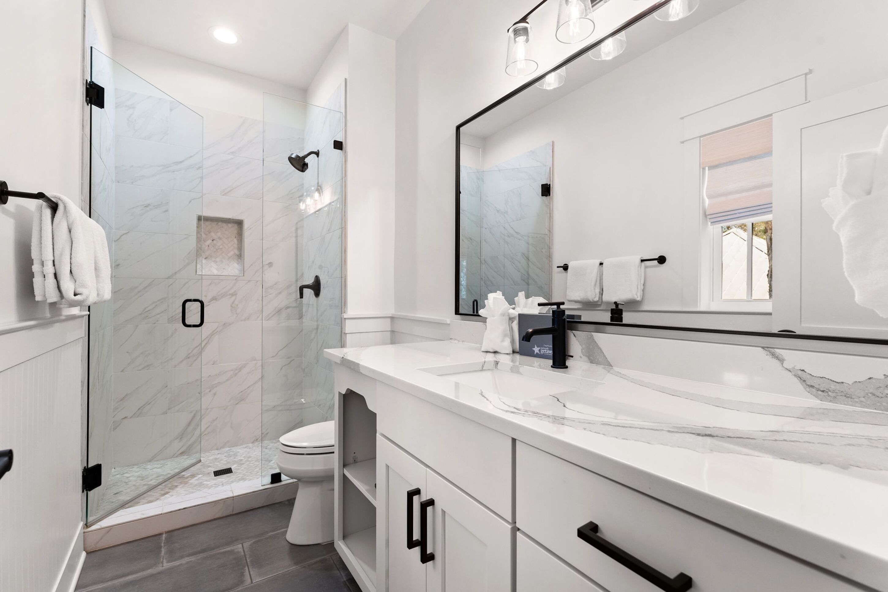 A modern bathroom with a glass-enclosed shower, a large mirror, and white marble countertops.